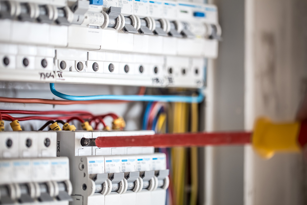 Man, an electrical technician working in a switchboard with fuses. Installation and connection of electrical equipment. Professional with tools in hand. concept of complex work, space for text.